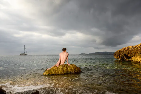 A conceptual photograph titled Siren 2/3 by Arjan Spannenburg featuring a nude man on a rock in the sea.