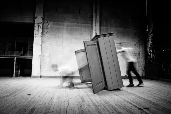 The Artwork COMING OUT : showing a blurred figure transitioning out of a wardrobe in a high-contrast black and white fine art photograph by Arjan Spannenburg.
