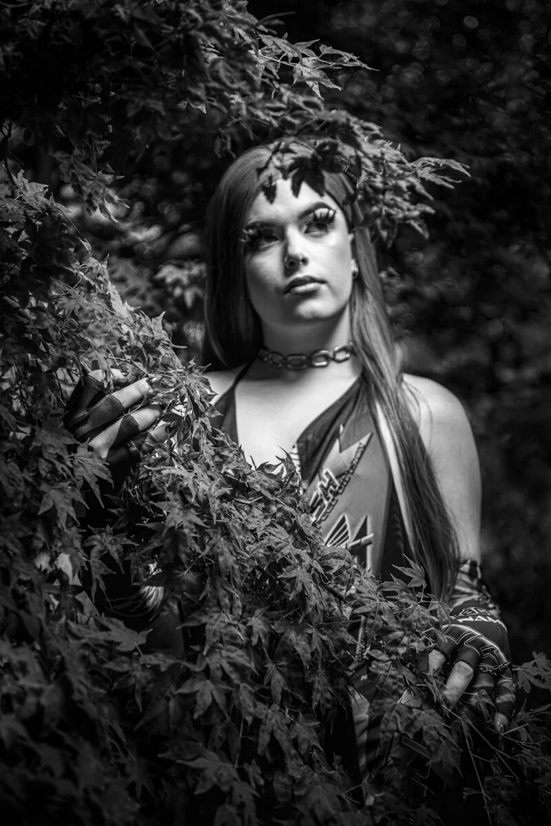 A black and white conceptual fine art portrait of LUX for the ESTRANGED series by ARJAN SPANNENBURG, featuring a person in drag among Japanese maple leaves.