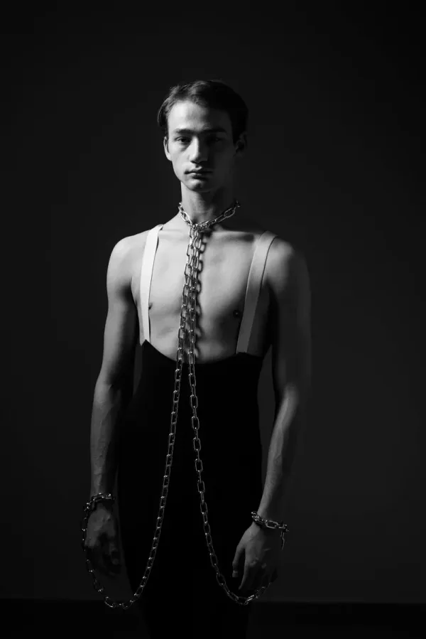 A vertical black and white portrait by ARJAN SPANNENBURG titled BOUND II, showing a man facing the camera with a direct gaze and heavy chains around his neck and wrists.