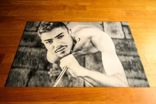 A black and white high-contrast floor installation from the Compelled series by Arjan Spannenburg, depicting a muscular man gripping a chain and looking up at the viewer.
