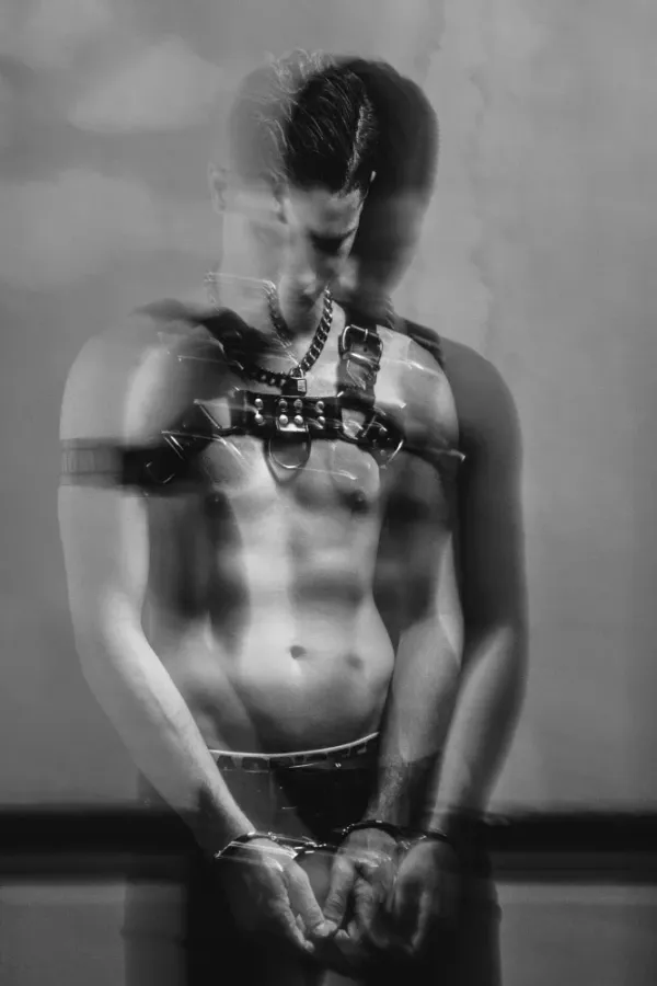 Black and white fine art photograph titled DESIRE by Arjan Spannenburg, featuring a muscular male torso with a leather harness and handcuffs, utilizing motion blur to represent identity.