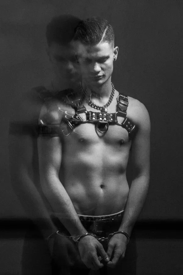 A high-contrast black and white photograph by Arjan Spannenburg titled WORRIED, featuring a man in a leather harness and handcuffs with a downward gaze and a blurred secondary exposure.