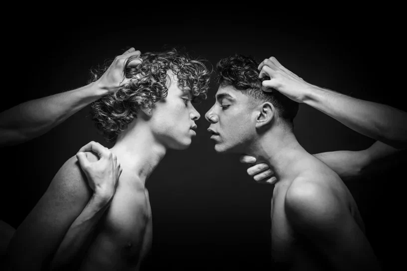 A high-contrast black and white conceptual photograph by Arjan Spannenburg titled Restraint, depicting two men attempting to connect while being physically held back by multiple anonymous hands.